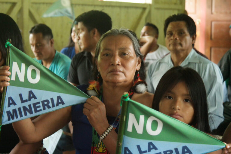 At an assembly, the president of the Shuar Arutam People shows banners saying “No to mining.”