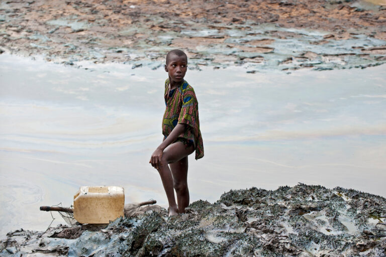 A boy with a fishing net stands on the crude oil-stained bank of a rift in the creek area in Niger Delta.