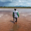A paddy field farmer wades through his agricultural land flooded with red mud.