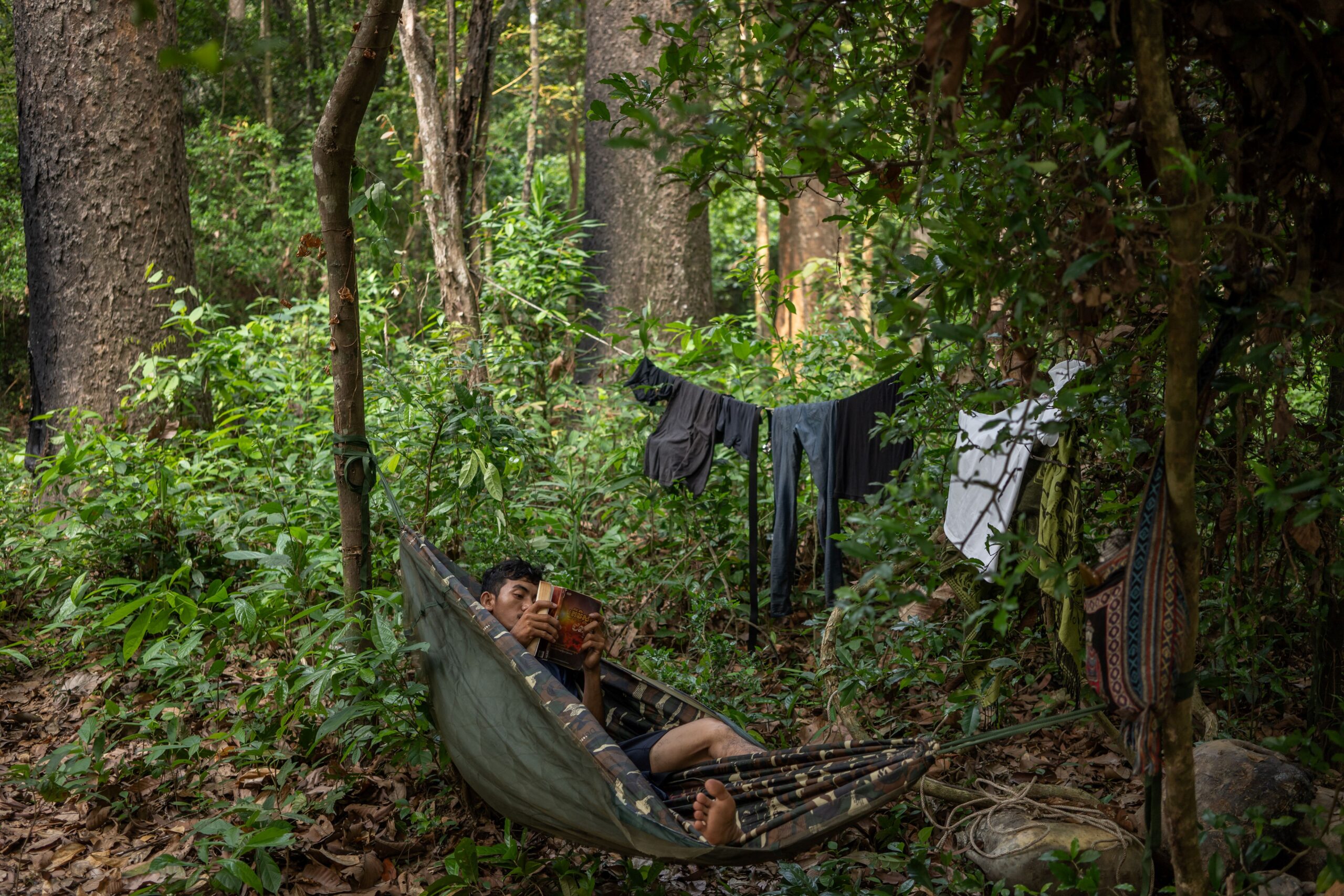 A member of the Prey Preah Roka Community Network reads a book at the makeshift camp one morning before the patrol resumes its path through the protected forest. Image by Andy Ball / Mongabay.