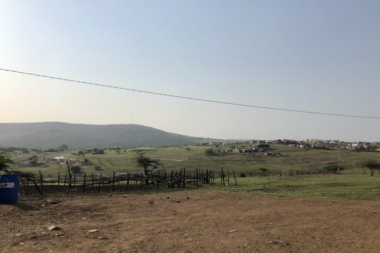 Wide shot of scattered buildings on green hills, a mountain on the horizon. Image by Victoria Schneider for Mongabay.